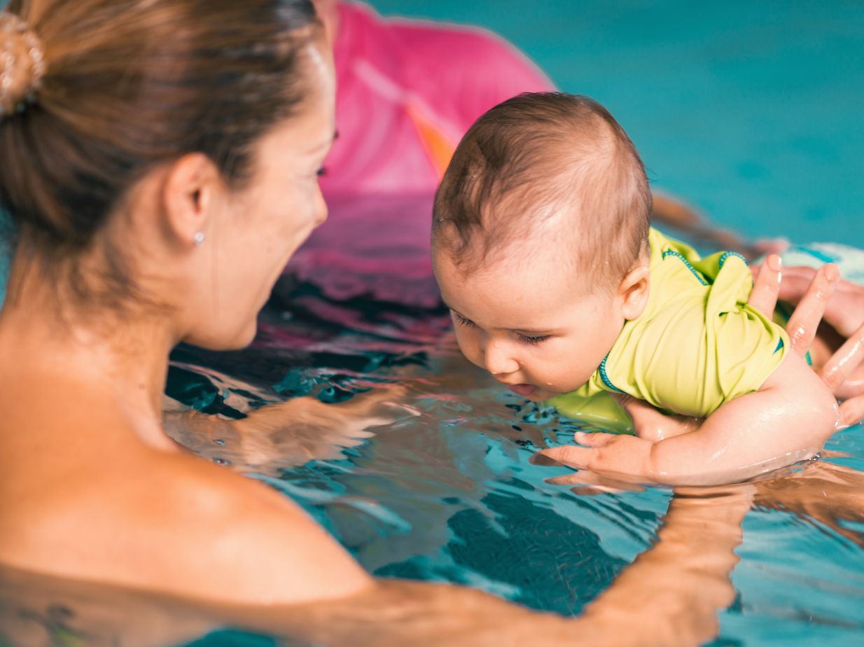 Bebé nadando hacia los brazos de su madre, en una piscina. La natación mejora la respiración en bebés
