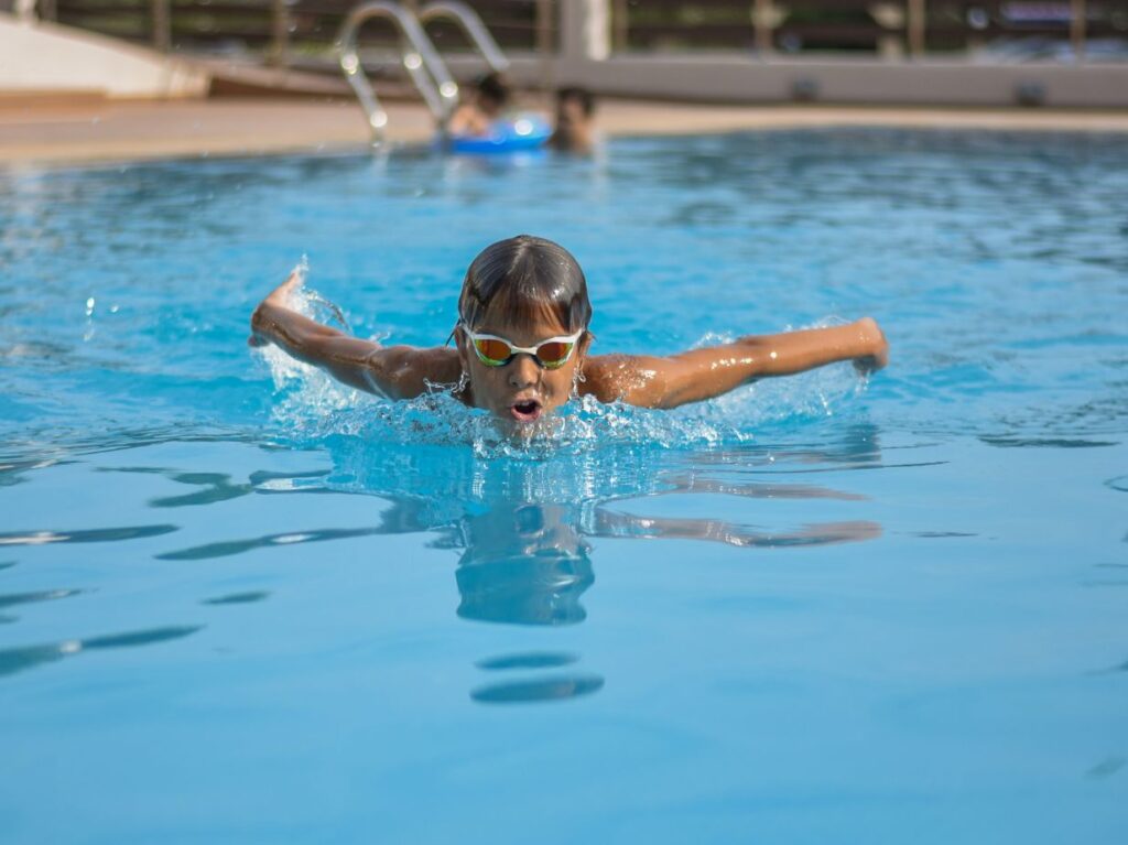 Niño nadando el estilo mariposa de natación, en una alberca al aire libre