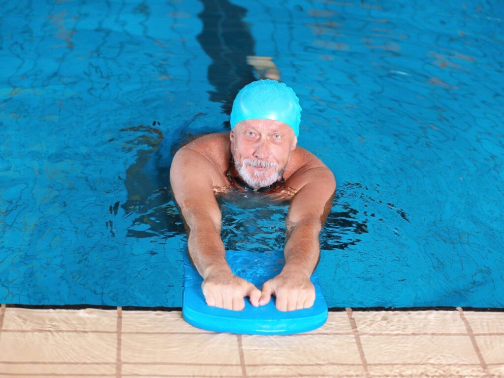 Hombre mayor en una piscina, con una tabla de nadar