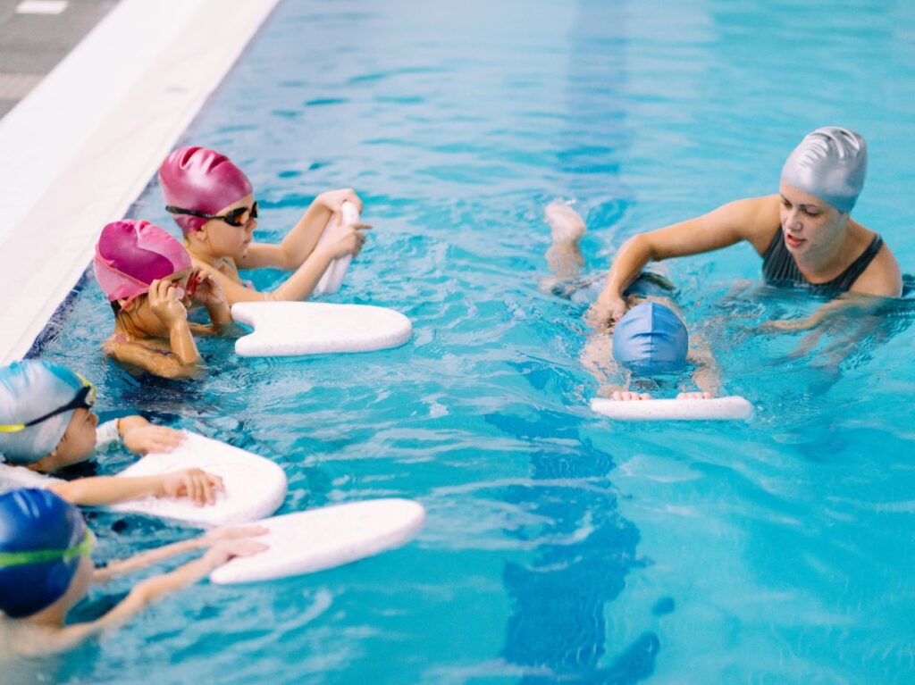 Un grupo de niños y niñas, tomando clases de natación para niños con miedo al agua, con una maestra
