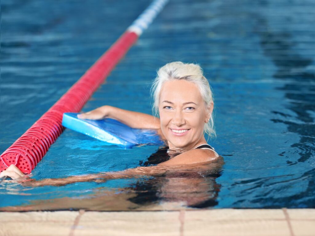Señora en una alberca, después de una clase de natación, disfrutando de los beneficios de la natación para adultos mayores con artritis