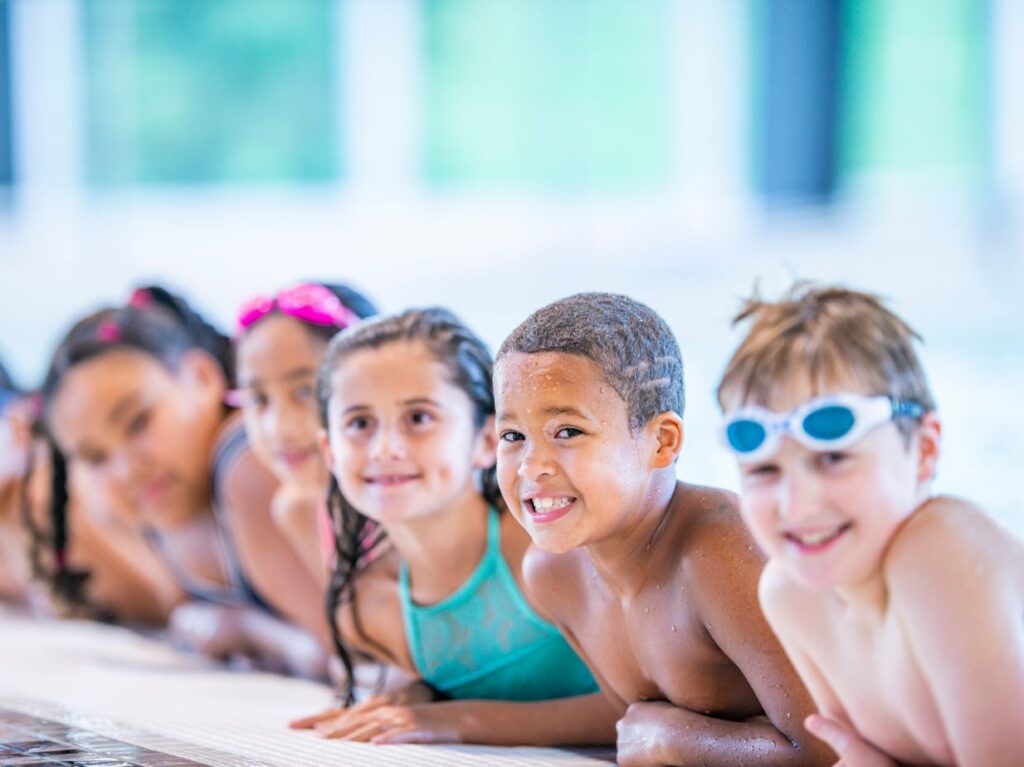 Un grupo de niños en la orilla de una piscina, contentos por sus clases de natación